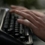 Close-up of hands typing on an old-fashioned typewriter, evoking nostalgia and creativity.